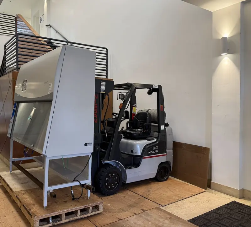 Biosafety cabinet staged on a reinforced custom pallet next to a forklift on plywood floor protection in a Bay Area biotech lobby