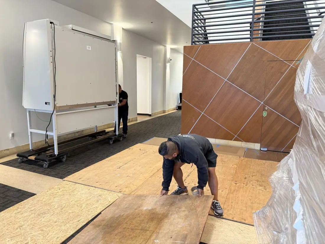 Ontrack Moving crew member handling floor protection sheets in a Bay Area biotech building lobby, with a biosafety cabinet on dollies in the background