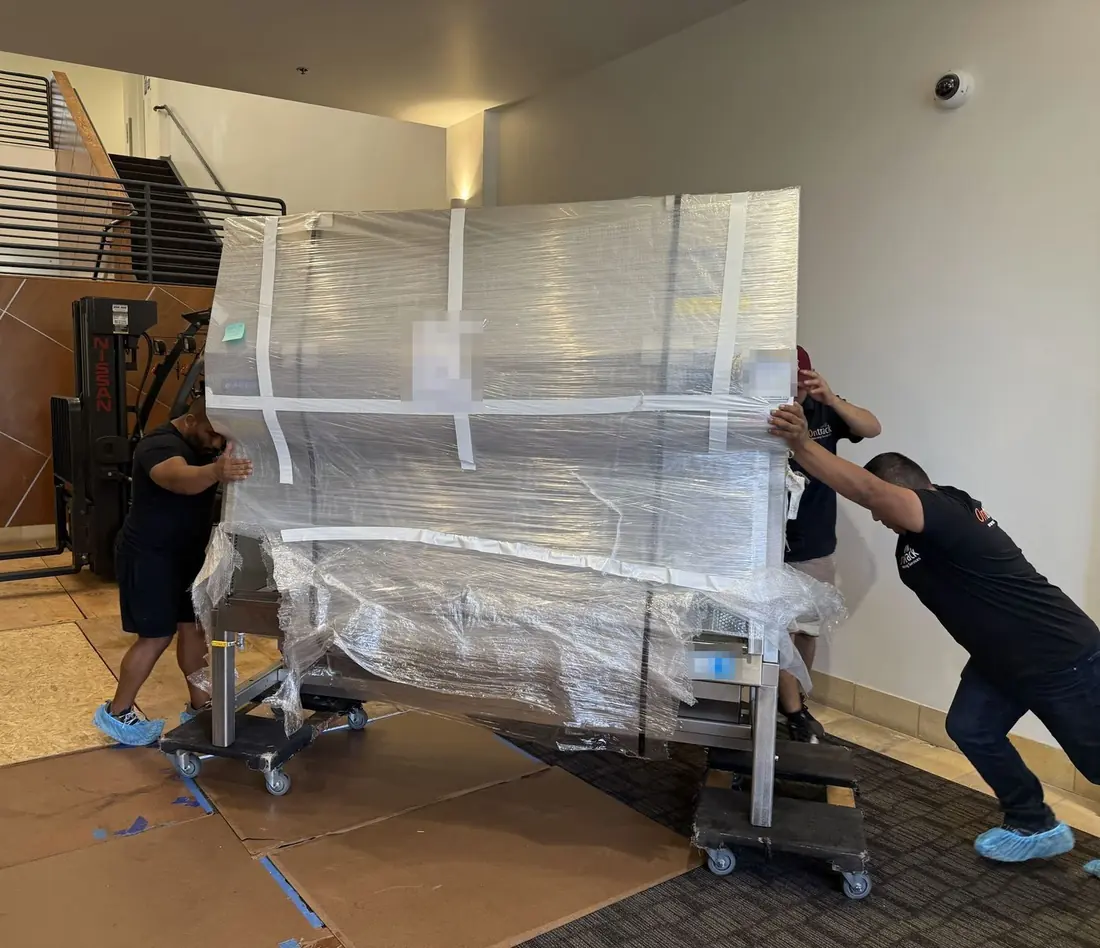 Plastic-wrapped biosafety cabinet on dollies pushed across Masonite floor protection by Ontrack Moving crew wearing shoe booties during a clean lab move