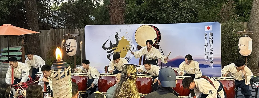 Hero's Club Yamato taiko drummers performing outdoors in front of a Yamato backdrop during their Bay Area tour, with drums transported by Ontrack Moving