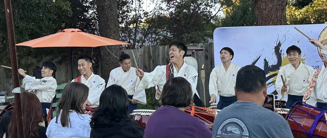 Taiko drummers in white kimono-style tops and hakama playing nagado-daiko drums at an outdoor Bay Area show during the Yamato Project USA ZERO tour
