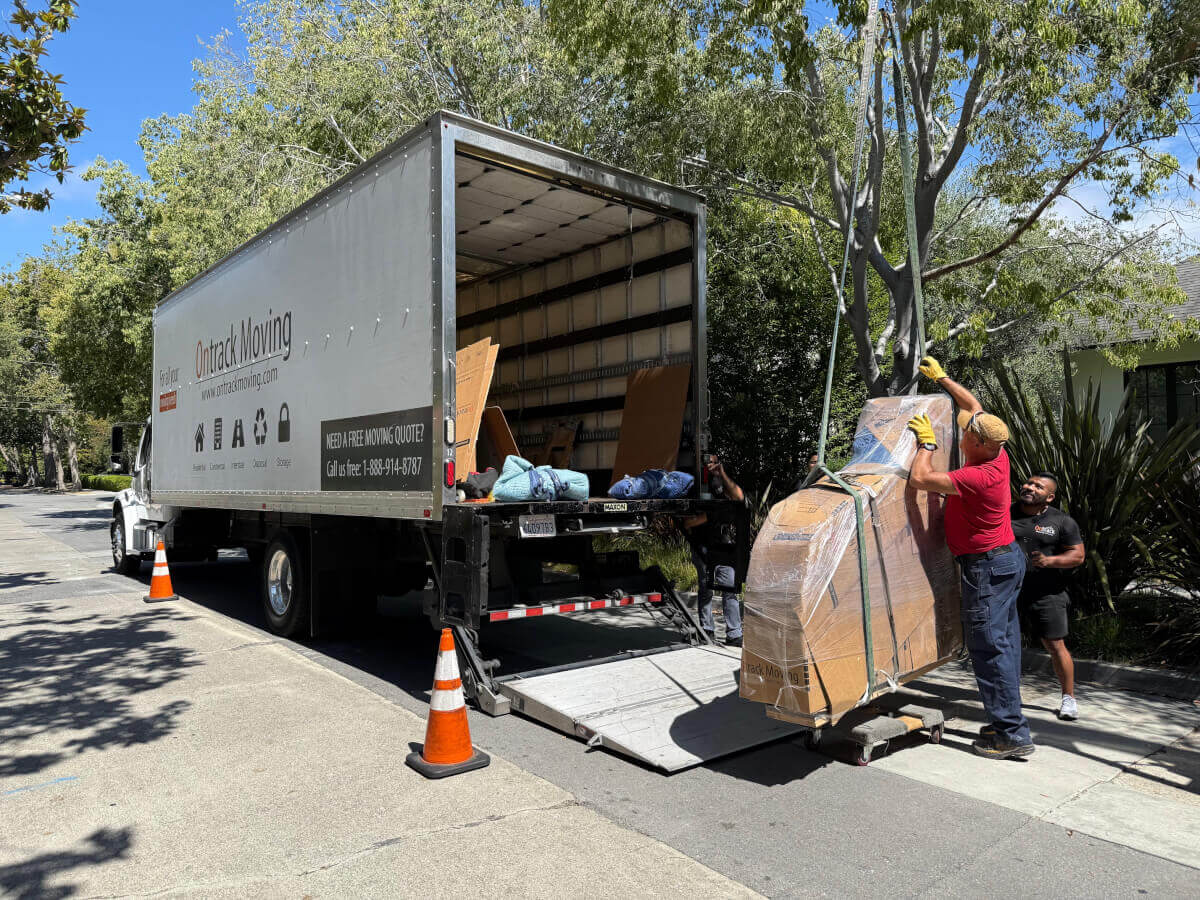Ontrack Moving crew loading wrapped grand piano onto branded truck via liftgate