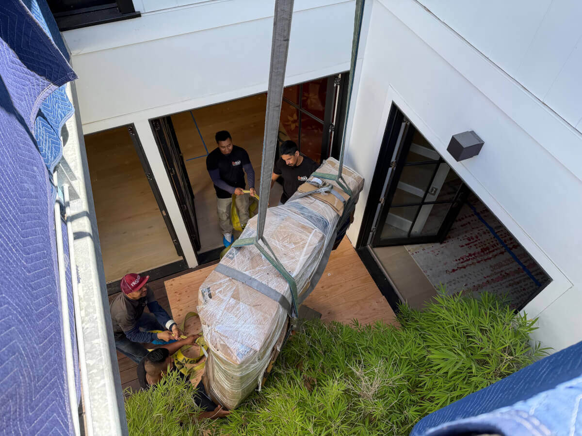 Ontrack Moving crew maneuvering wrapped grand piano through doorway with heavy-duty straps