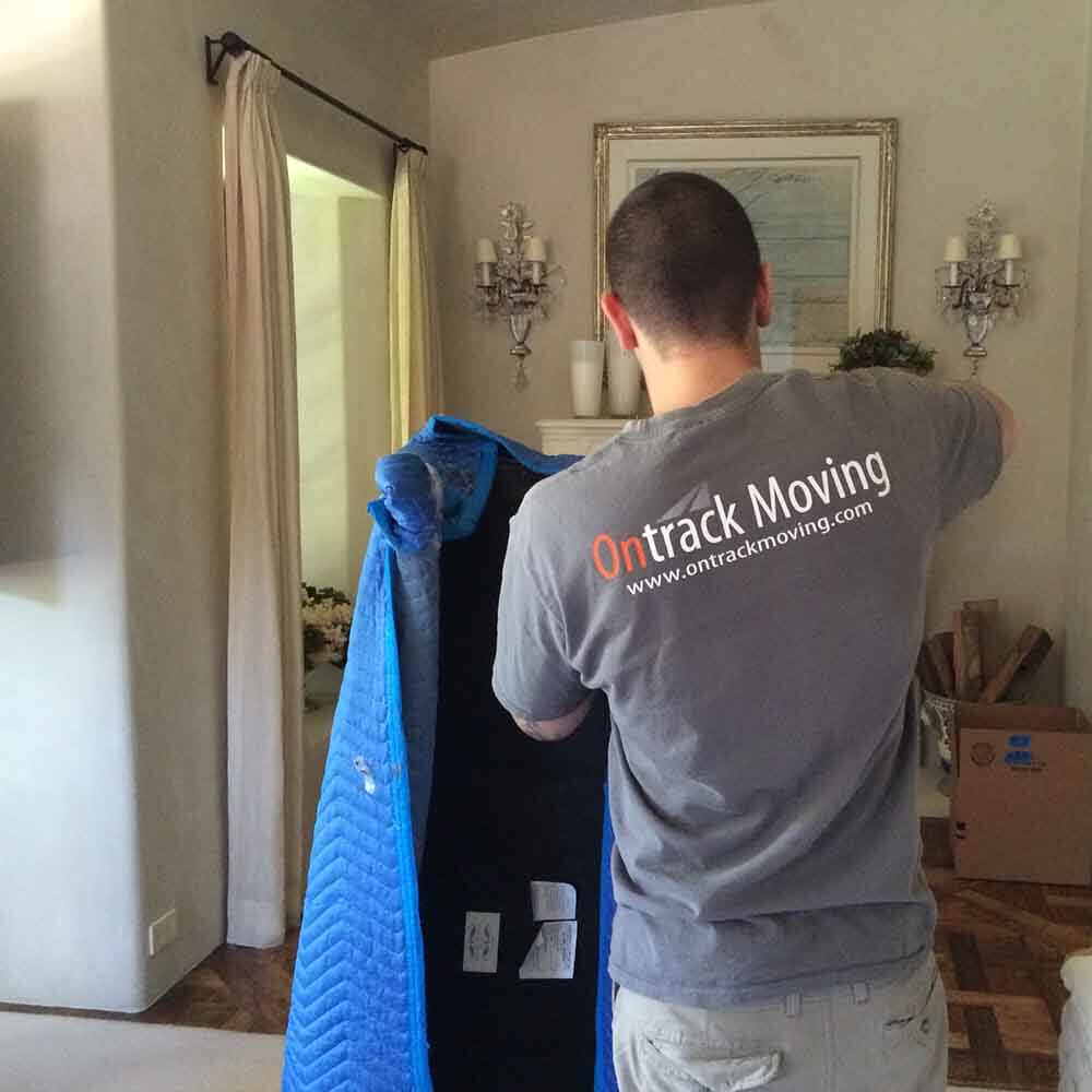 Ontrack Moving crew member wrapping bedroom furniture in a quilted moving blanket inside a Bay Area home